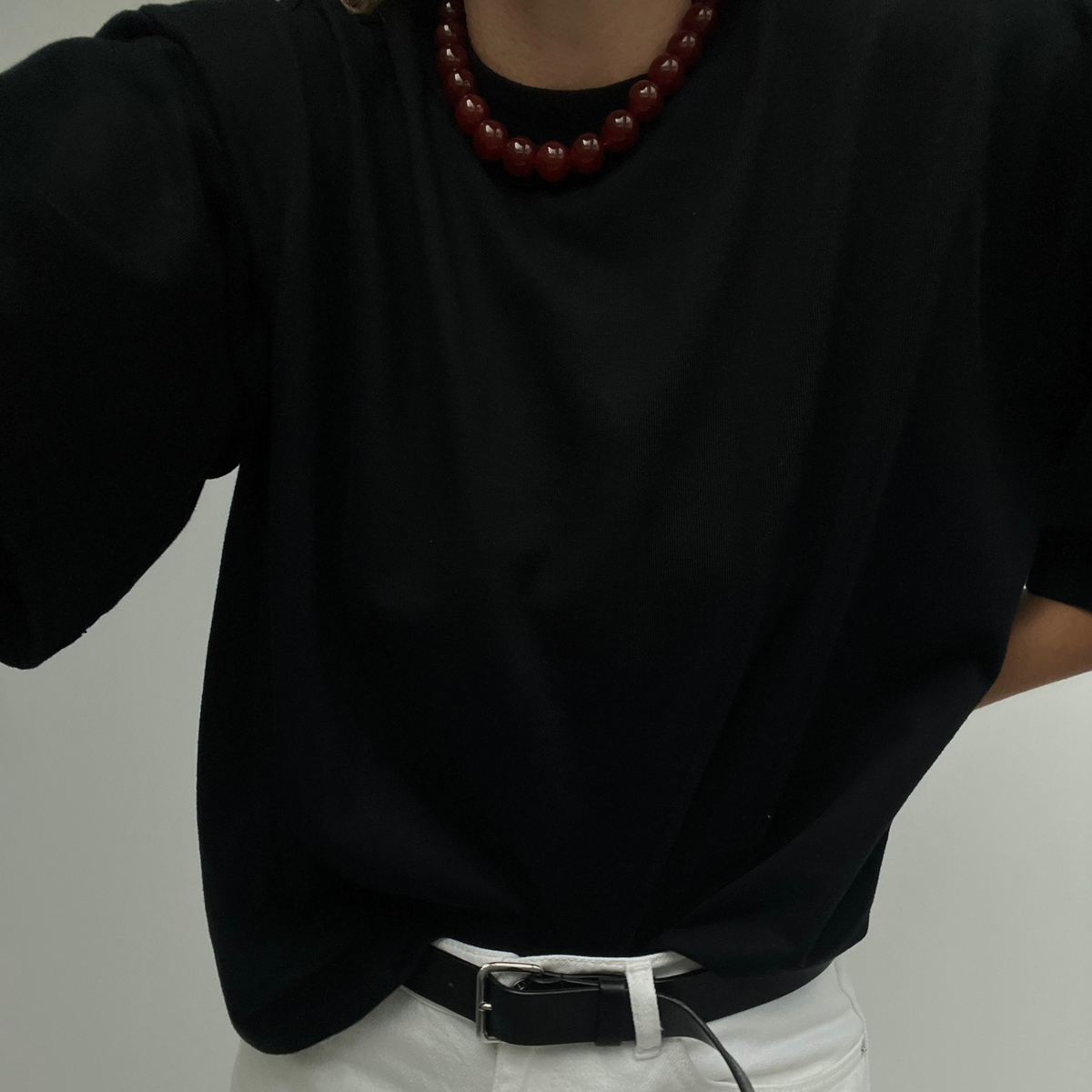 Person wearing a bold Carnelian necklace styled with a black oversized t-shirt tucked into white trousers, finished with a black belt — a minimal, confident look.