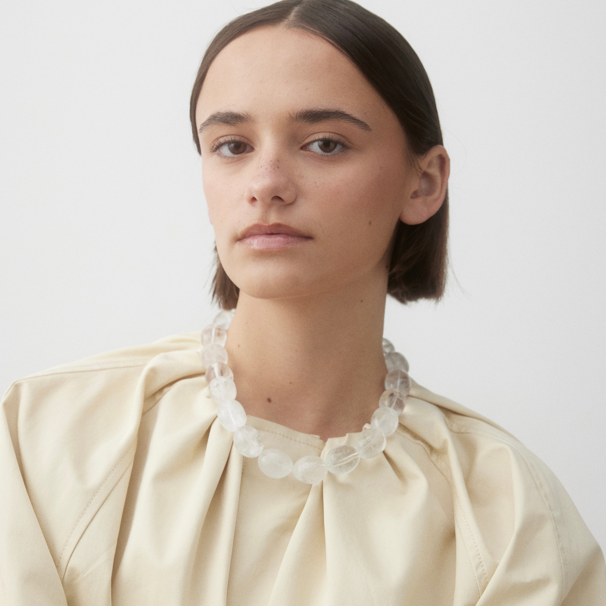 Woman wearing the Ignite Clear Quartz necklace with large oval clear quartz beads, styled with a soft cream blouse and a minimal, clean aesthetic.