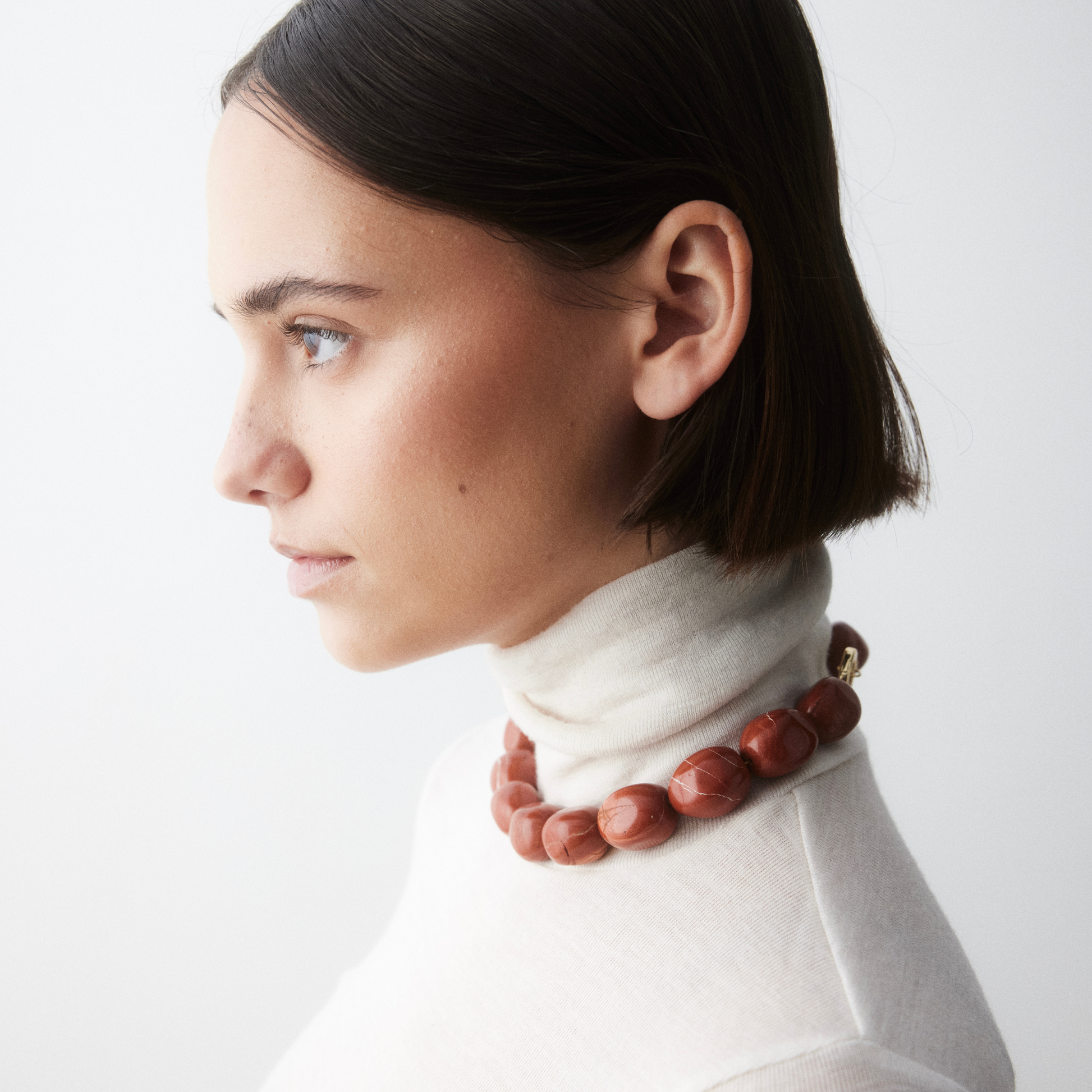 Side view of woman wearing the Ignite Red Jasper necklace by Stellar Whispers, styled over an off-white turtleneck to highlight the bold, grounding energy of the red crystal beads.