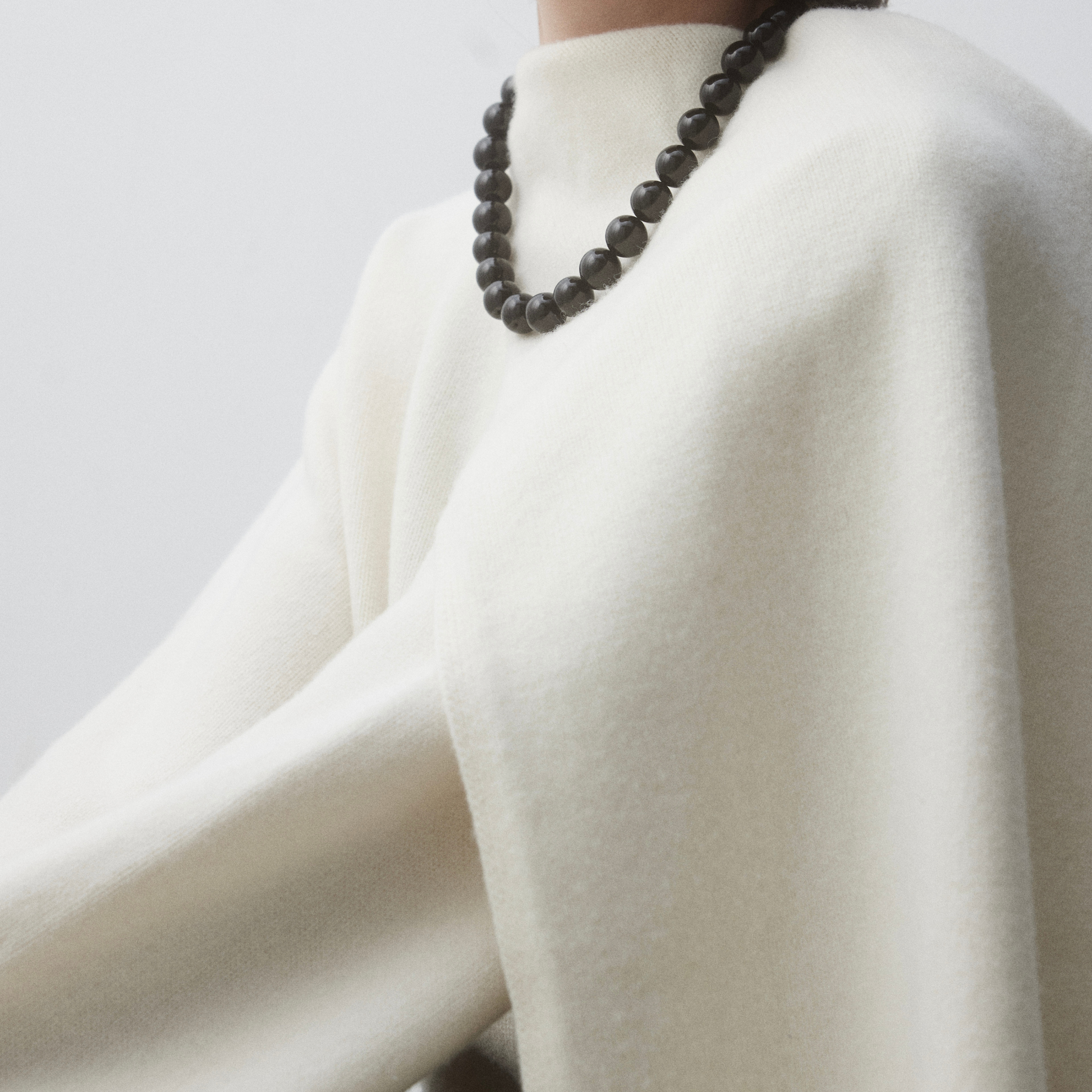 Close-up of the Grace Black Onyx Necklace styled over a soft off-white sweater, showcasing the bold, glossy 16mm black onyx beads against a minimal, elegant background.