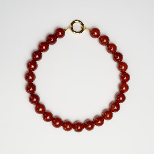 Grace Carnelian Necklace with polished deep red carnelian beads and a gold clasp, arranged in a circle on a white background.