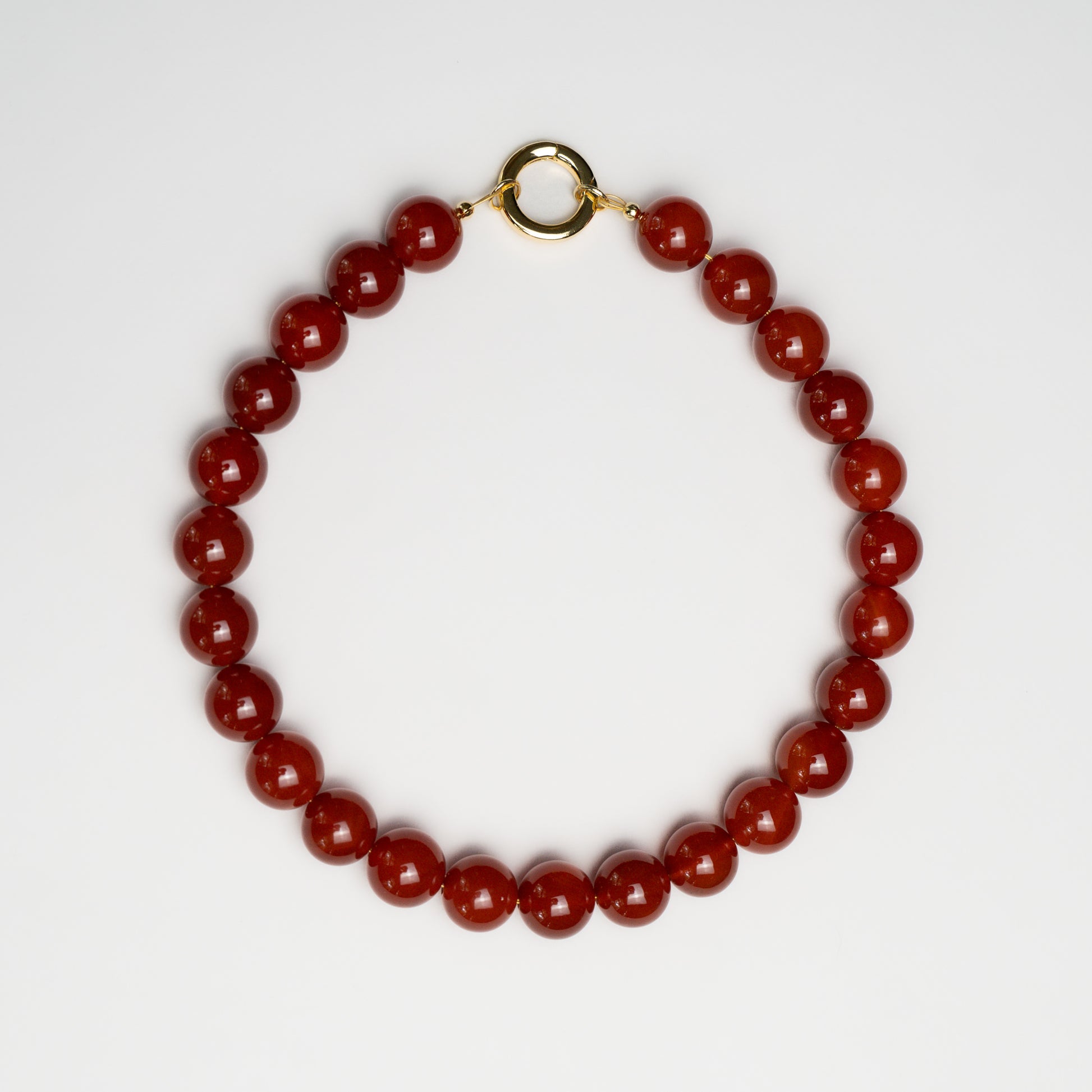 Grace Carnelian Necklace with polished deep red carnelian beads and a gold clasp, arranged in a circle on a white background.
