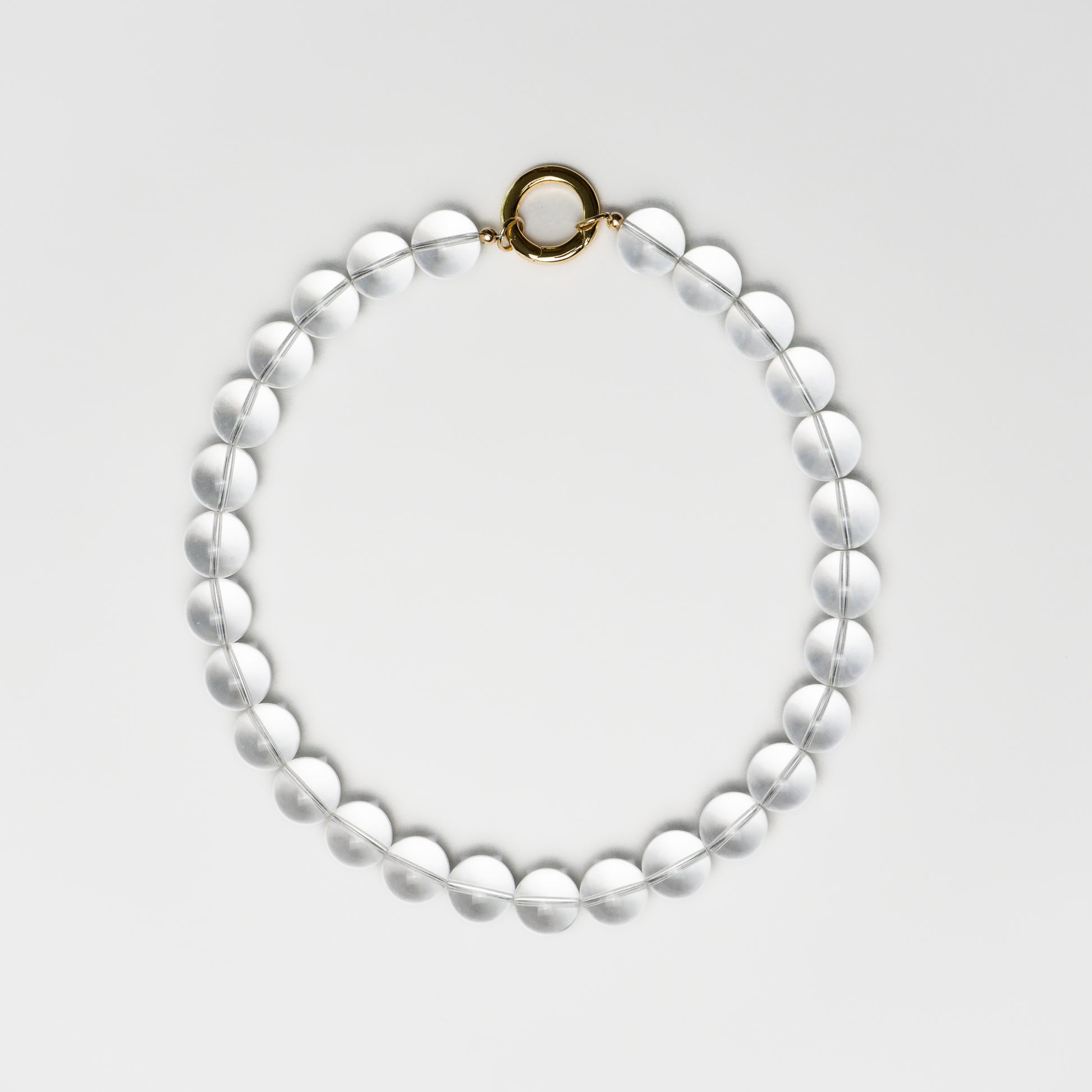 Clear Quartz bead necklace with a round gold clasp, laid flat in a circular shape on a white background.